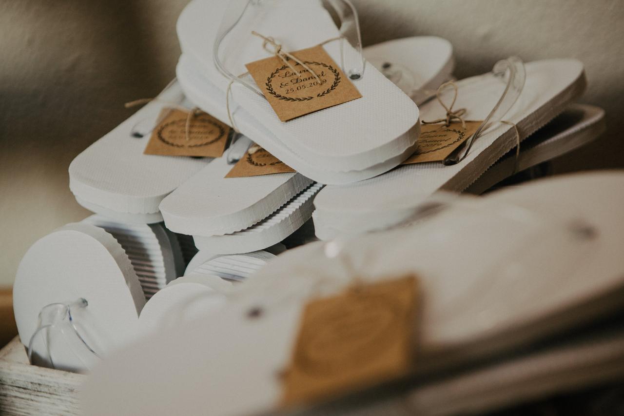 Chanclas blancas con tiras transparentes con una etiqueta en papel kraft con los nombres de la pareja que se va a casar y la fecha del enlace