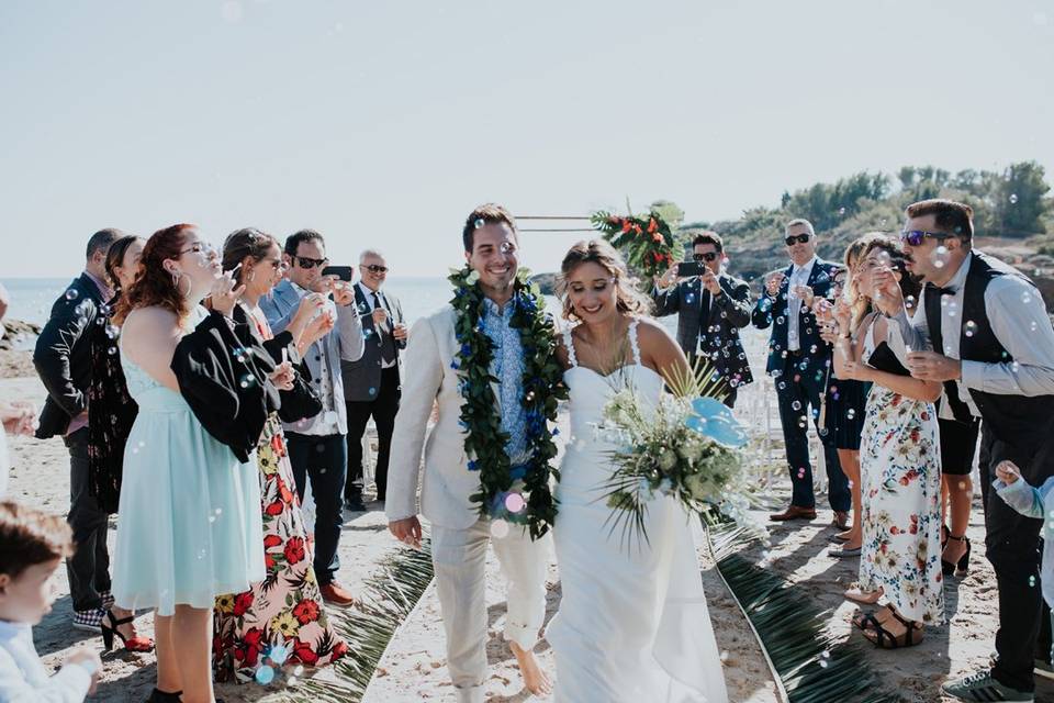 Pareja de novios saliendo de la boda en la playa con los invitados en el pasillo