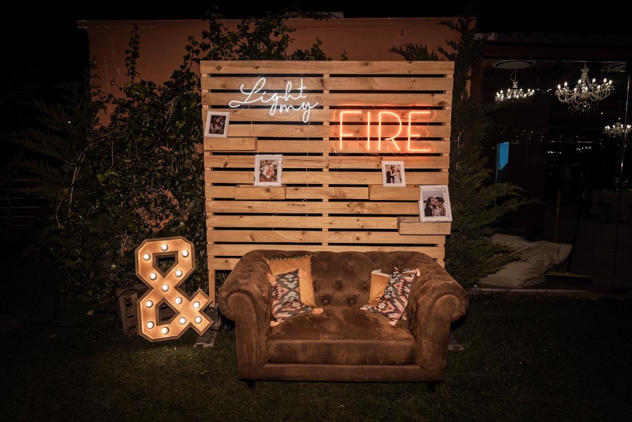 montaje del photocall de boda con un sofá envejecido, luces de neón, fotos, cojines y un fondo de madera