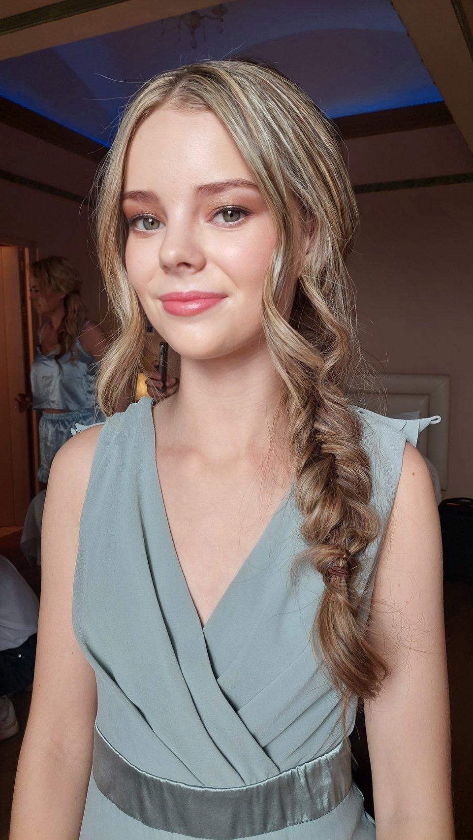 Recogidos invitada boda: mujer rubia con trenza lateral sonríe con un vestido en verde pastel