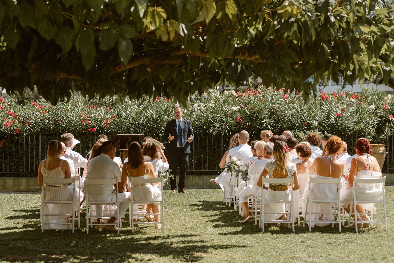 Lista invitado boda: ceremonia civil al aire libre con el oficiante de cara y todos los invitados vestidos de blanco de espaldas