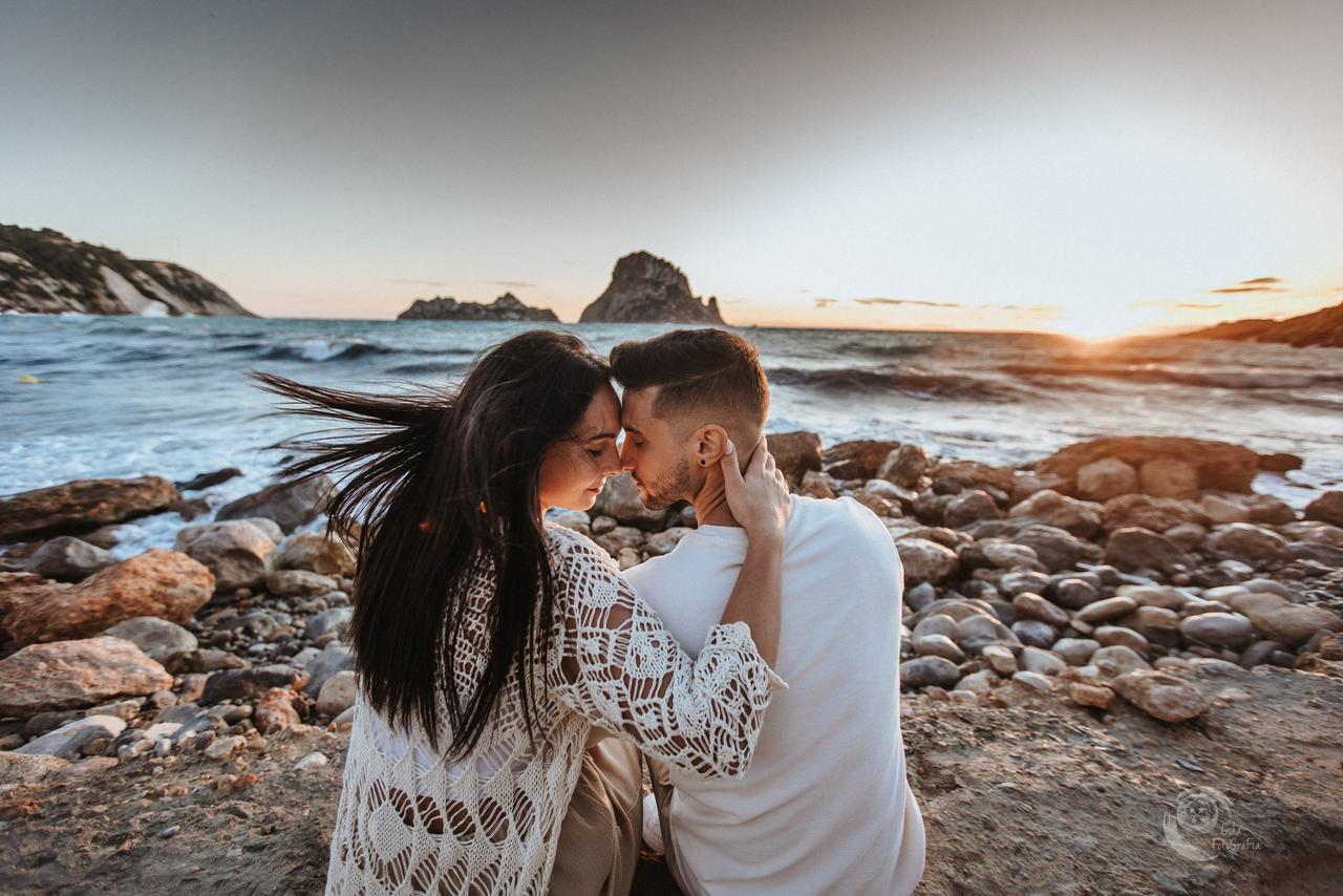 Lat relacionamento: menino e menina muito amorosos, sentados ao lado de algumas pedras à beira do mar, durante o pôr do sol
