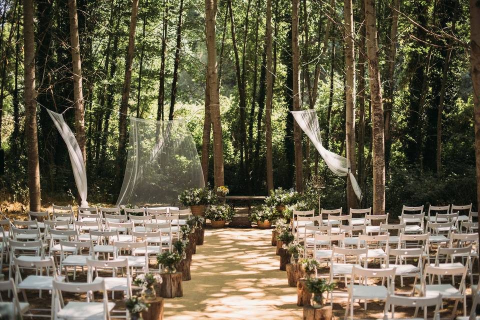 ceremonia de boda en un bosque con sillas blancas y telas a modo de arco