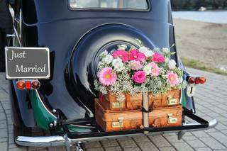 Coche clásico con una bandeja en la parte trasera con maletas antiguas y un bonito y colorido ramo de flores