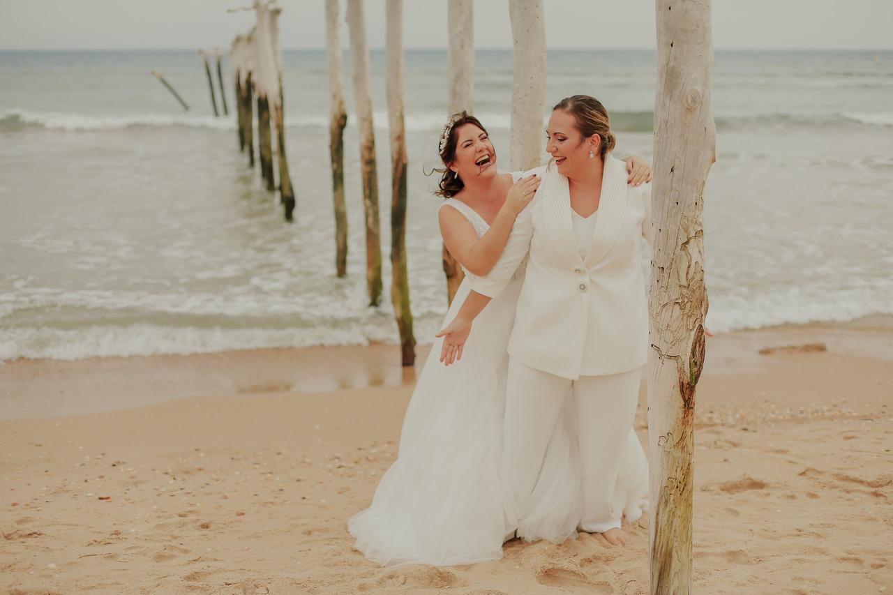 Dos chicas vestidas de novia posan muy naturales y sonrientes en una playa junto al mar