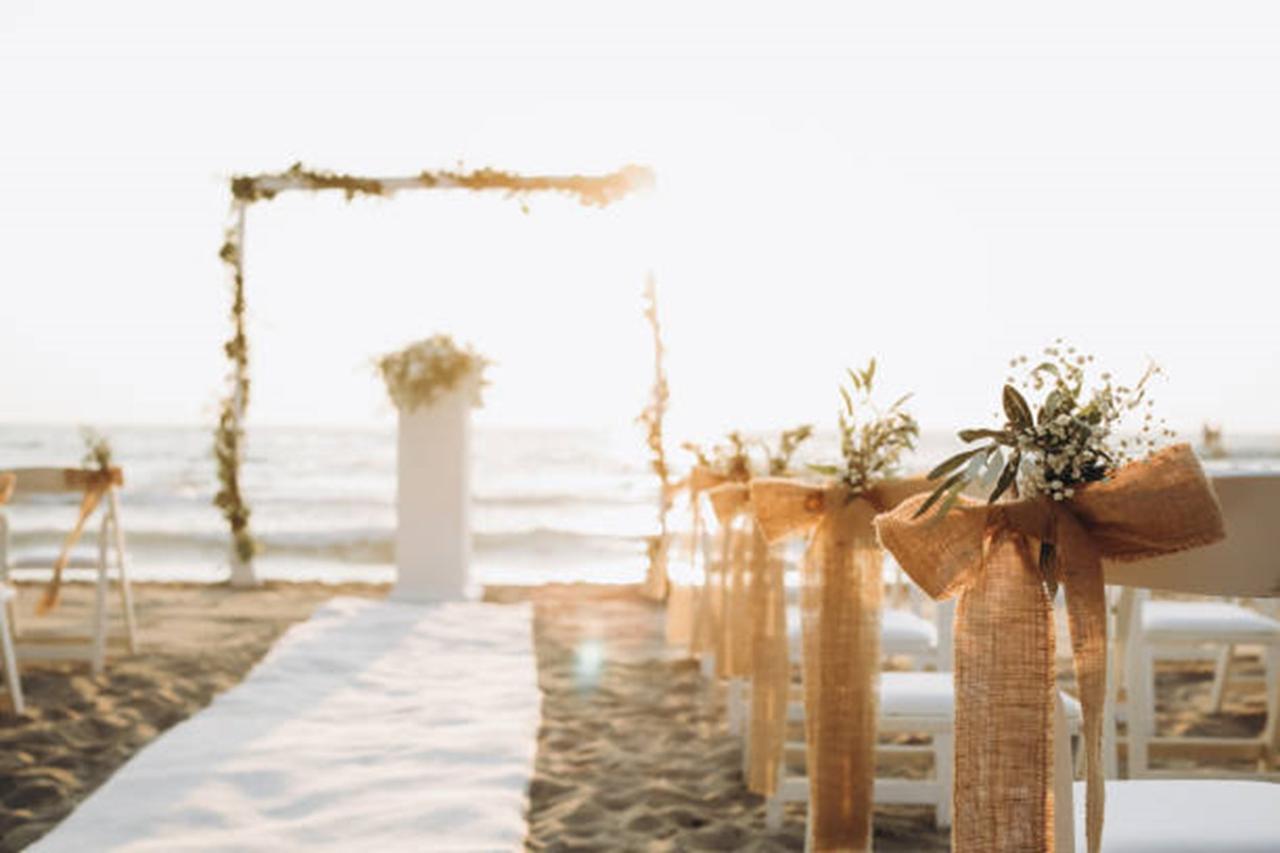 Decoración de bodas en la playa: sillas de la ceremonia decoradas con lazos hechos con tela y ramilletes de flores