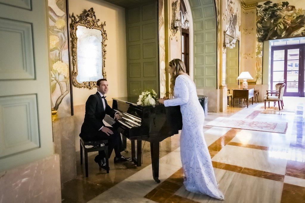 Hombre con traje oscuro y mujer con traje blanco en una elegante salón con piano