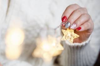 Mano femenina aguantando una estrella brillante con una manicura navideña en rojo, blanco y plata brillante