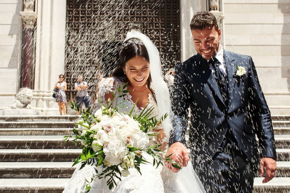 Matrimonio feliz: pareja de recién casados muy sonrientes saliendo de la iglesia mientras les tiran arroz