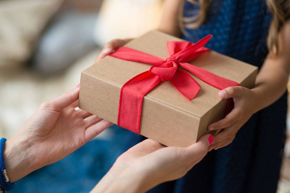 Manos cogiendo un paquete de regalo de Navidad con lazo rojo