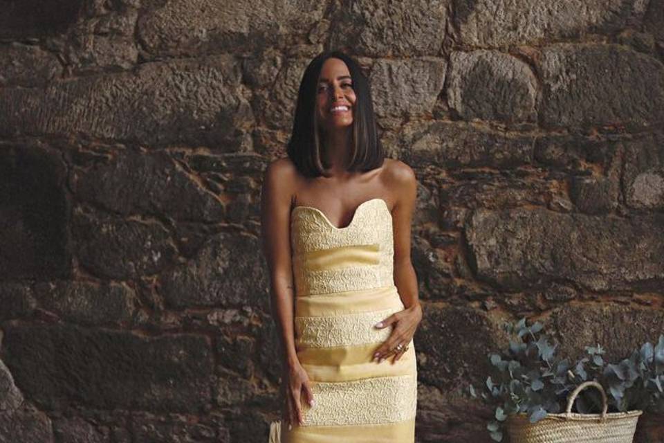 La influencer María Fernández Rubíes con un elegante vestido de invitada amarillo con un escote corazón muy sugerente en un fondo de piedra natural