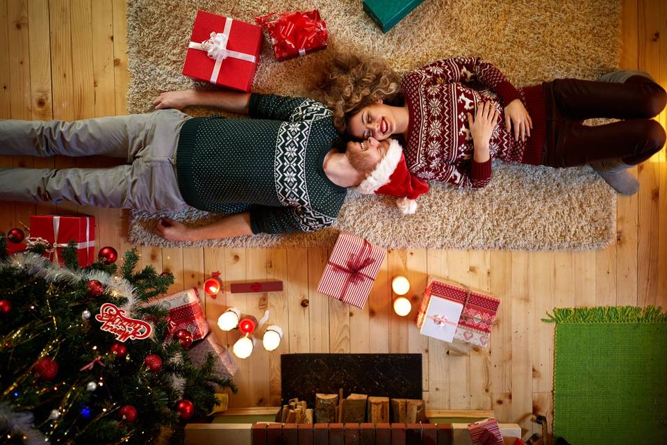 Pareja sonriente estirada en el suelo junto al árbol de Navidad y varias cajas de regalos