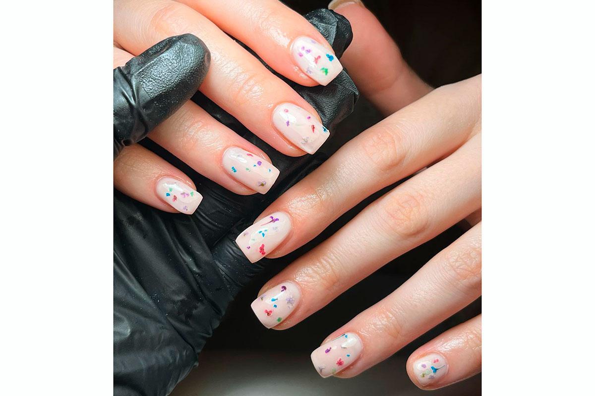 manos con manicura milky bath con flores secas de colores