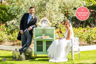 Chico vestido de novio y chica vestida de novia en un rincón decorativo al aire libre con muebles y elementos vintage