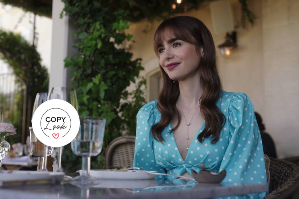 Look de Emily in Paris con Lilly Collins como protagonista sentada en una mesa con vestido de lunares azul con abertura