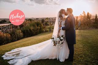 Pareja con traje y vestido de novia de besa en un precioso jardín durante la puesta de sol