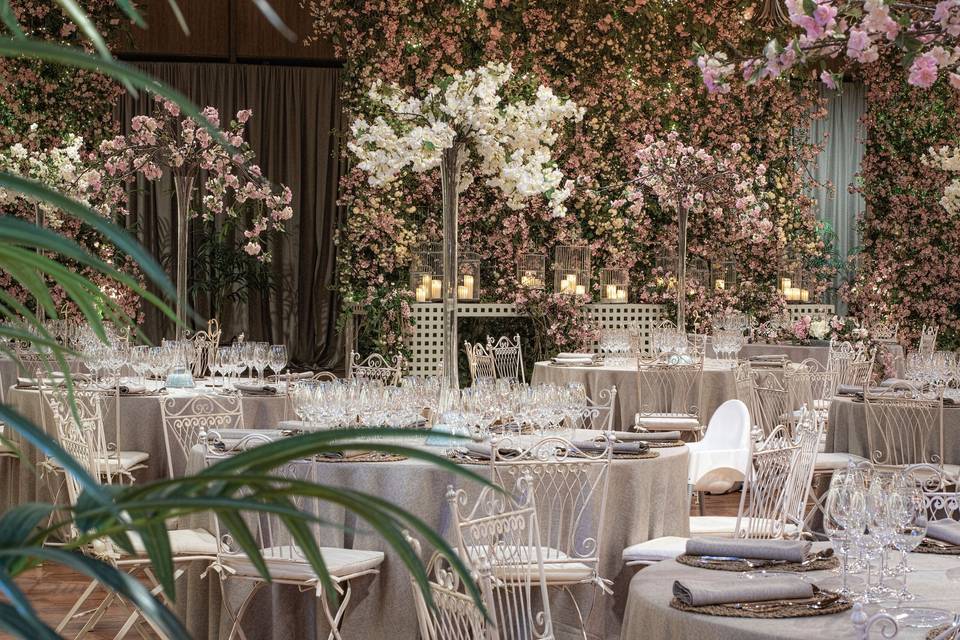 Precioso espacio con muchas flores, mesas redondas elegantemente vestidas para una comida o cena especial y sillas de forja