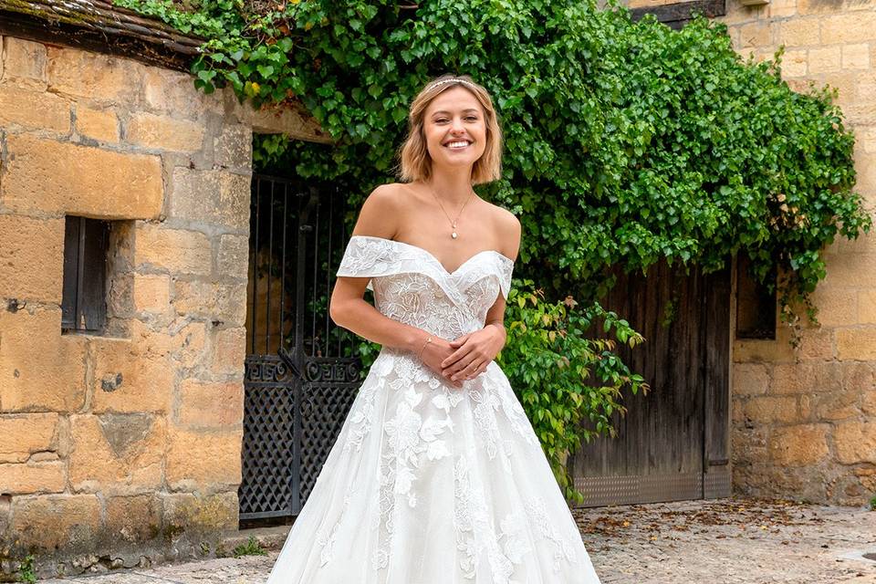 Chica muy sonriente con un vestido de novia con escote de hombros caídos y falda con volumen