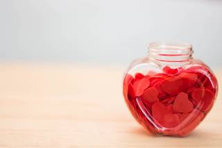 Tarro de cristal con forma de corazón con muchos corazones rojos en su interior