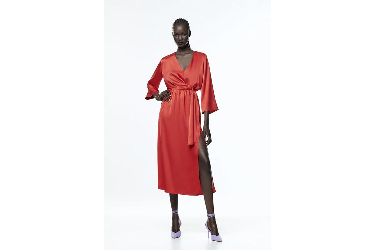 Chica negra con zapatos rosas de tacón y vestido rojo de acabado satinado con manga francesa y abertura en la falda