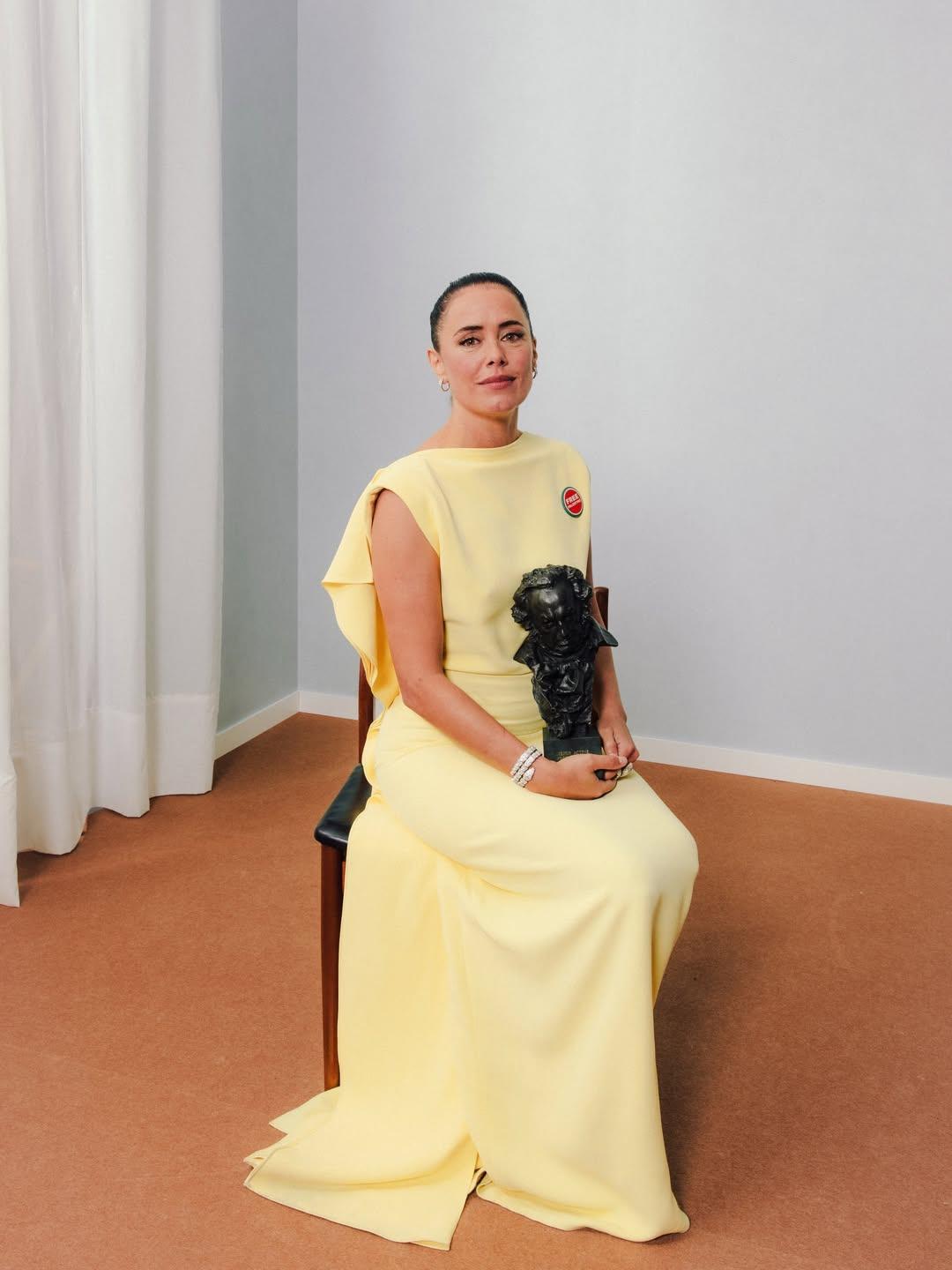Patricia López actriz estatua goya con vestido invitada loewe amarillo pastel sentada en una silla