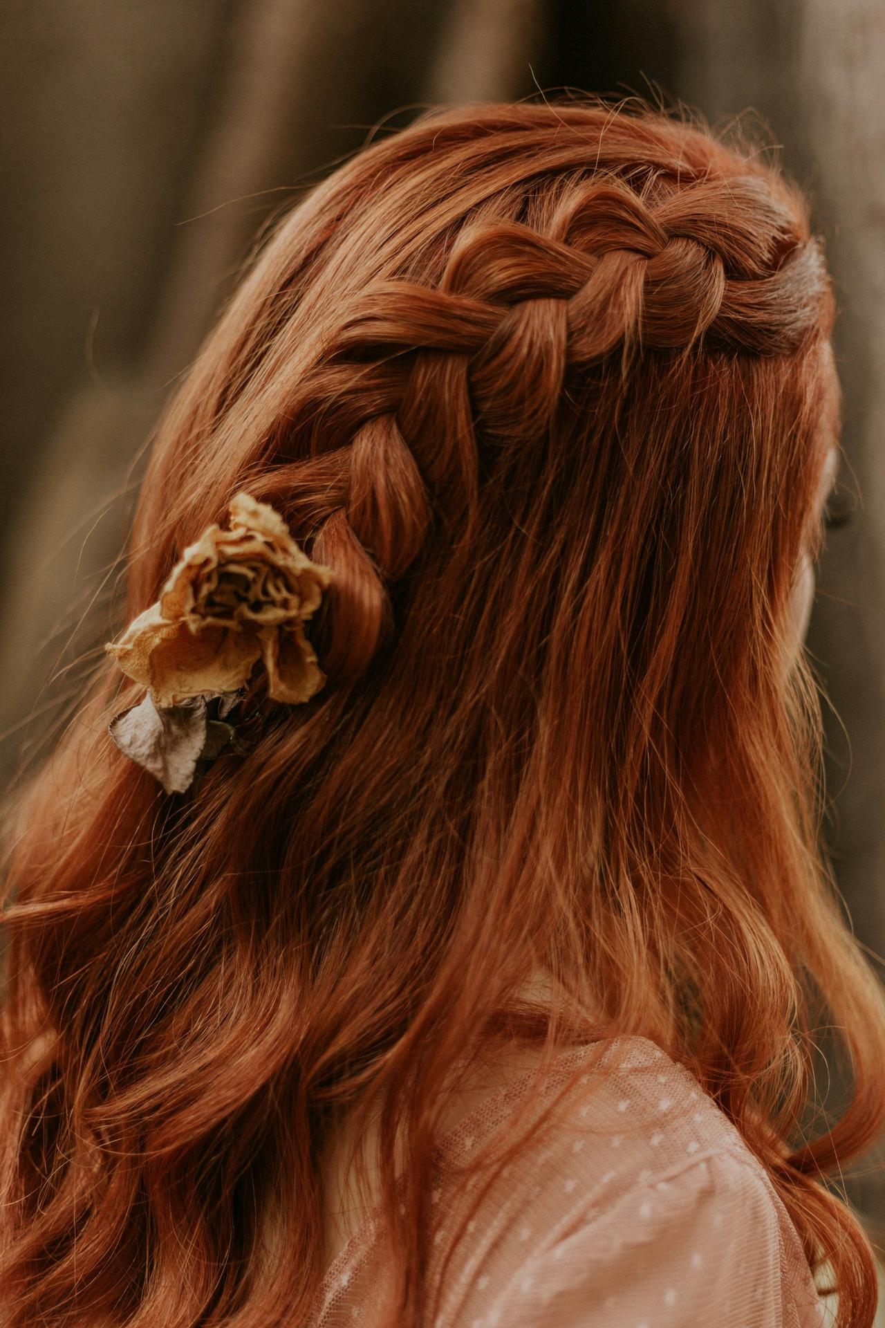 peinados trenzas boda: Melena pelirroja suelta con trenza lateral y detalle floral en el extremo