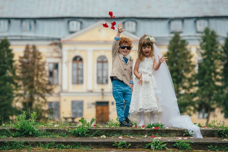 Pajes de boda revoltosos o vergonzosos: niño con americana lanzando pétalos de flores rojos y niña con vestido blanco divertida