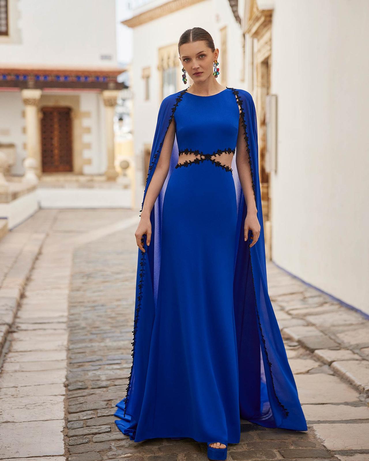 Vestidos invitada boda primavera: vestido azul añil largo con aberturas en la cintura y capa desde los hombros