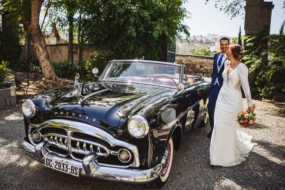 Coches descapotables antiguos para bodas aparcado al lado de una pareja vestida de novios muy sonriente