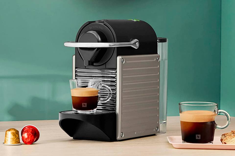 Cafetera Nespresso en negro y metal con varias tazas de café y cápsulas de colores