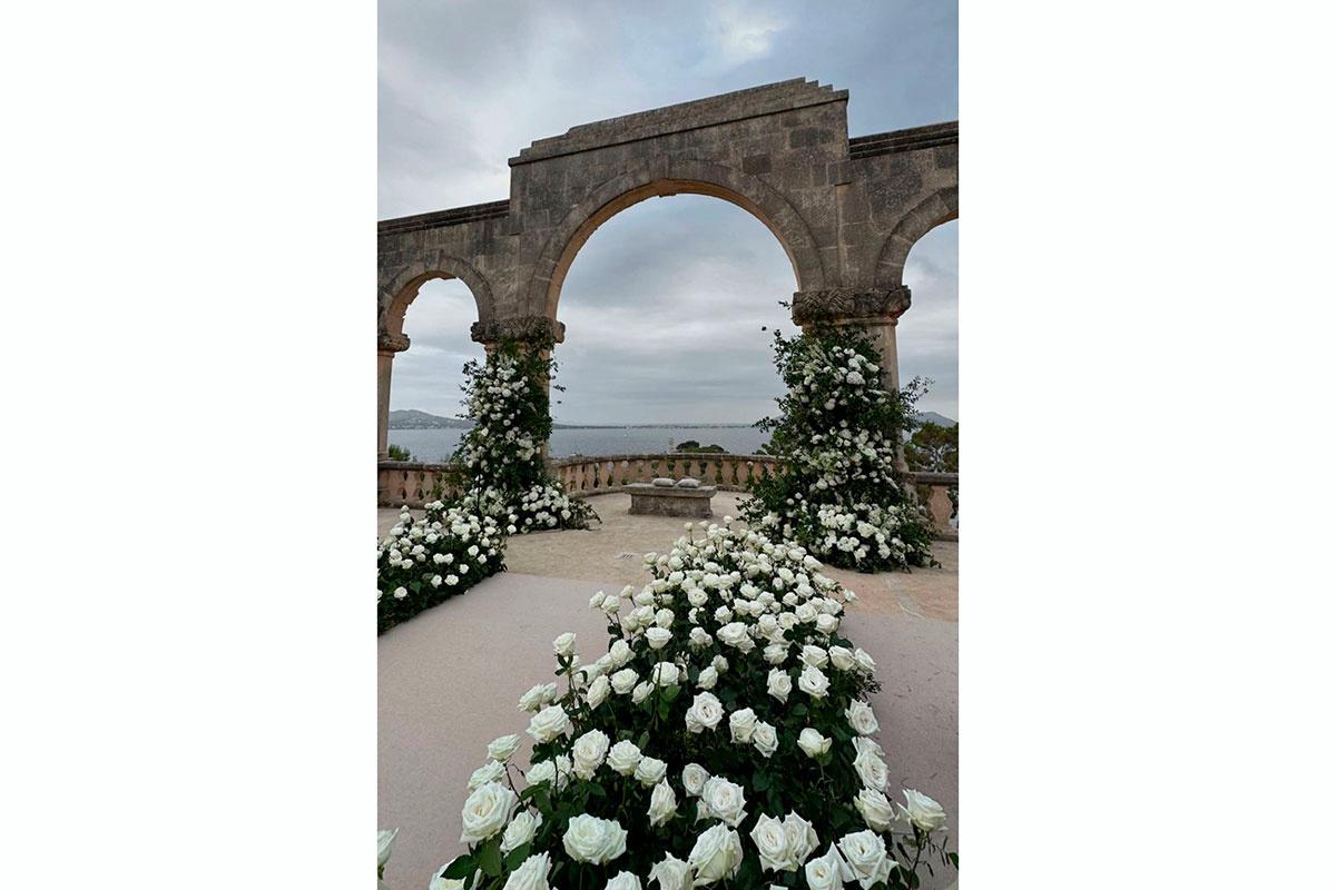 rosas blancas decoran el pasillo nupcial hacia un altar frente a mar bajo arcos de piedra