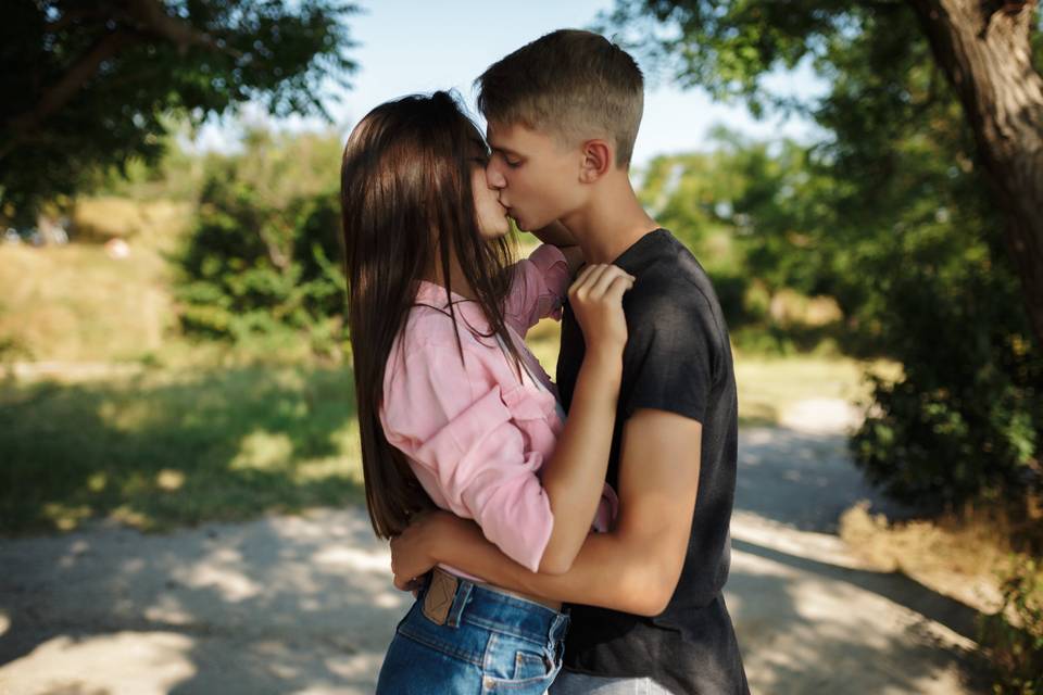 Chico y chica muy jóvenes se abrazan y besan en medio de un parque - amor adolescente 