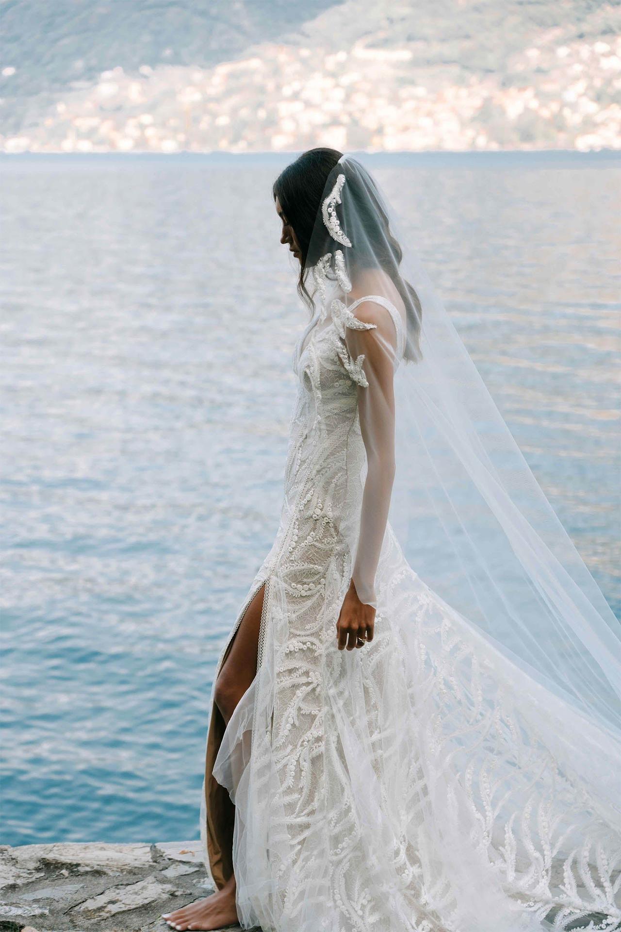 Chica morena junto al mar con un vestido y velo de novia