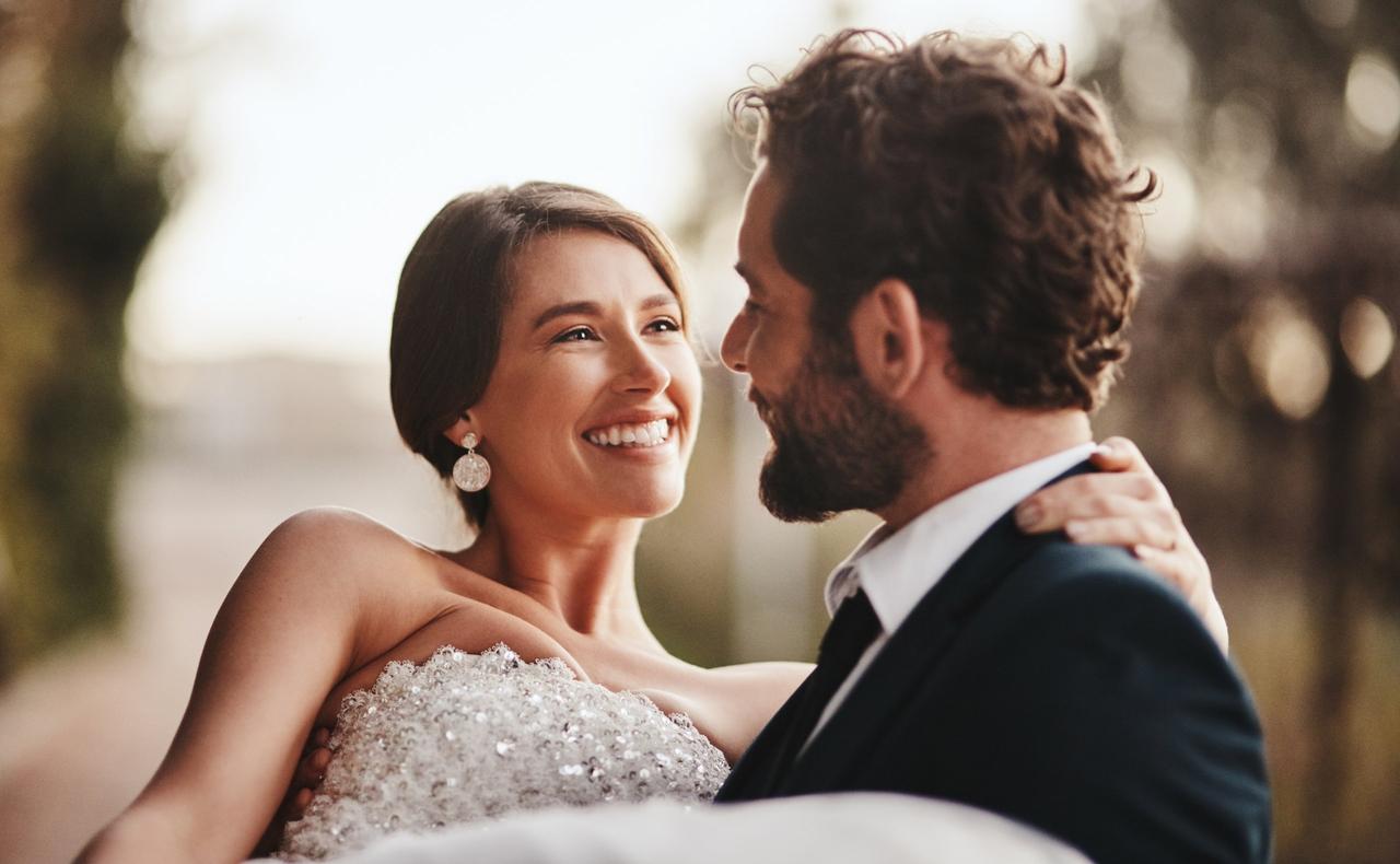 Cosas que las novias olvidan hacer el día de su boda: pareja de recién casados se miran enamorados mientras el chico sujeta a la chica en sus brazos