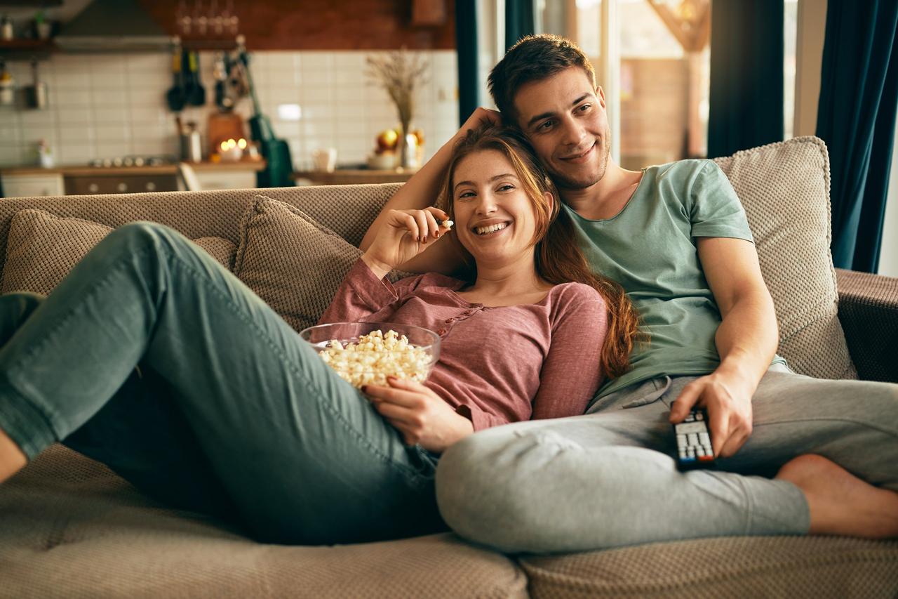 Pareja relajada en el sofá de casa viendo la tv con palomitas