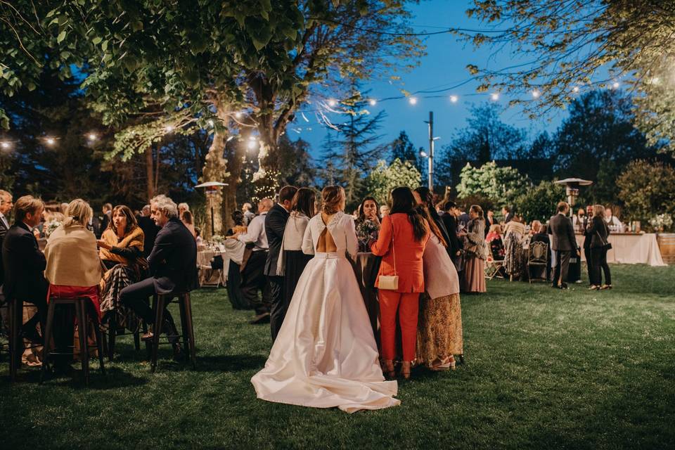 Invitados a una boda: banquete nupcial en un jardín con la novia en primer plano de espaldas hablando con algunos de los invitados