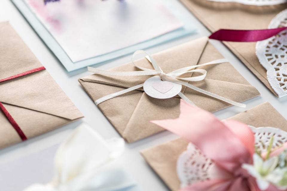 Invitaciones de boda caseras: sobres de papel kraft con cintas de colores y etiquetas con corazones