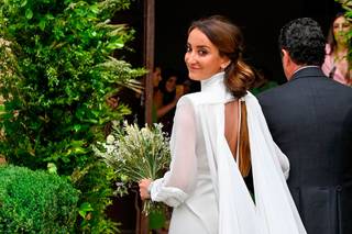 Lucía Pombo con su vestido de novia de espalda escotada y capa vaporosa entrando en un lugar cerrado