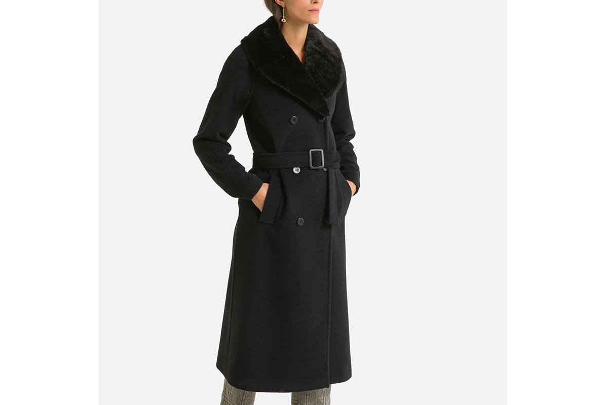 Chica con un abrigo largo negro con cinturón de anudar en la cintura y cuello de piel sintético