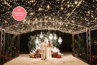 Precioso ambiente exterior con una pareja de novios de espaldas y una cuidada iluminación con lámparas y cielo estrellado