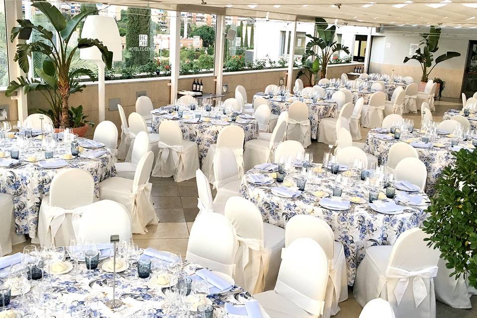 Espacioso salón con mesas redondas con mantelería en blanco y azul, y sillas con fundas blancas