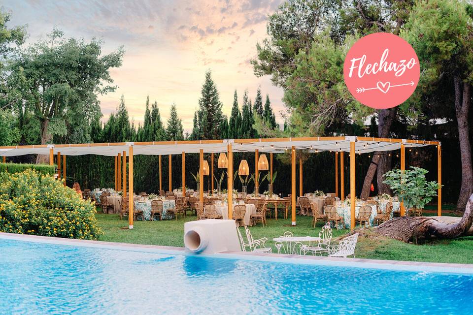 Montaje banquete de boda bajo una pérgola en un jardín al lado de una piscina en Masia Les Andanes