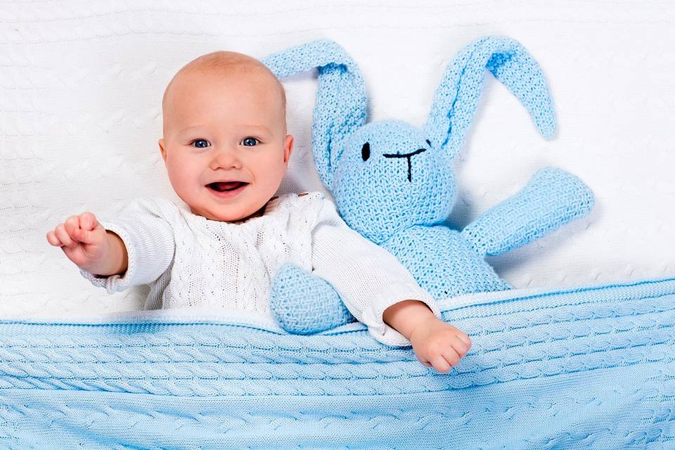 Marcas ropa bebé españolas: bebé muy sonriente en su camita con un conejito de color azul