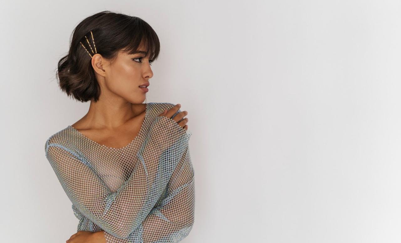 Peinados invitada boda pelo corto: mujer morena con pelo corto y horquillas doradas mira hacia un lado con los brazos sobre el pecho y una camiseta de red