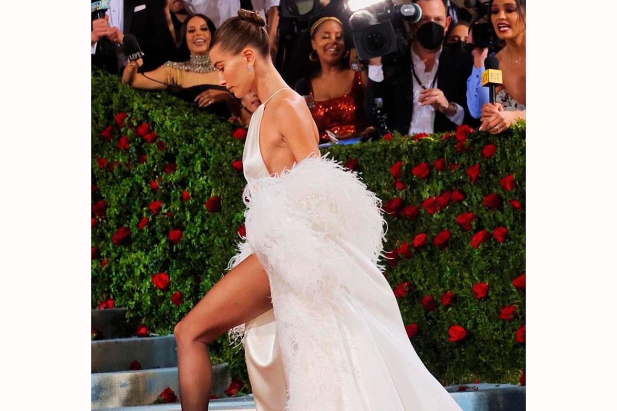 Hailey Biber en la alfombra roja de la gala del Met con un moño de bailarina alto y un vestido lencero blanco con plumas