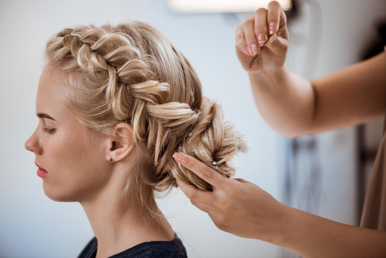 peinados trenzas boda: unas manos peinan a una mujer rubia nórdica con un recogido bajo con trenzas laterales.