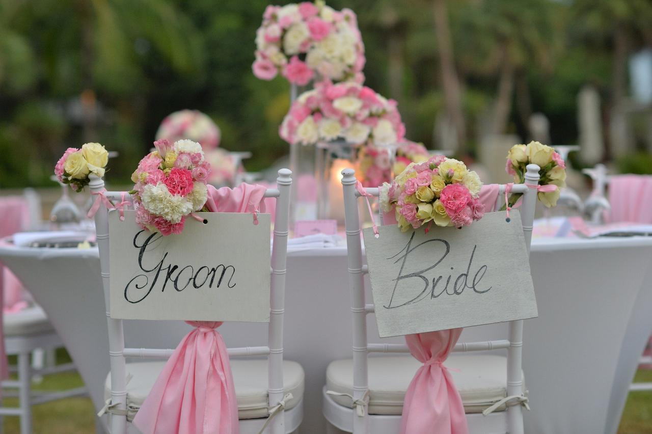 Sillas de los novios el día de la boda con carteles de groom y bride, cintas y composiciones florales