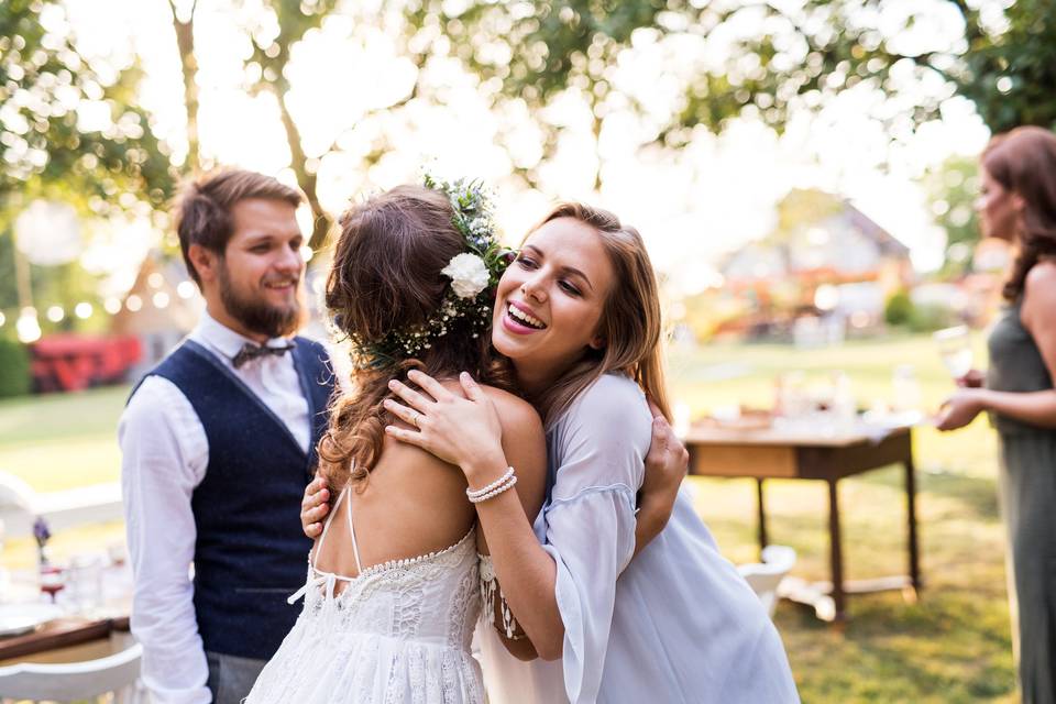 Chica rubia abrazando a una chica vestida de novia en un bonito jardín con césped