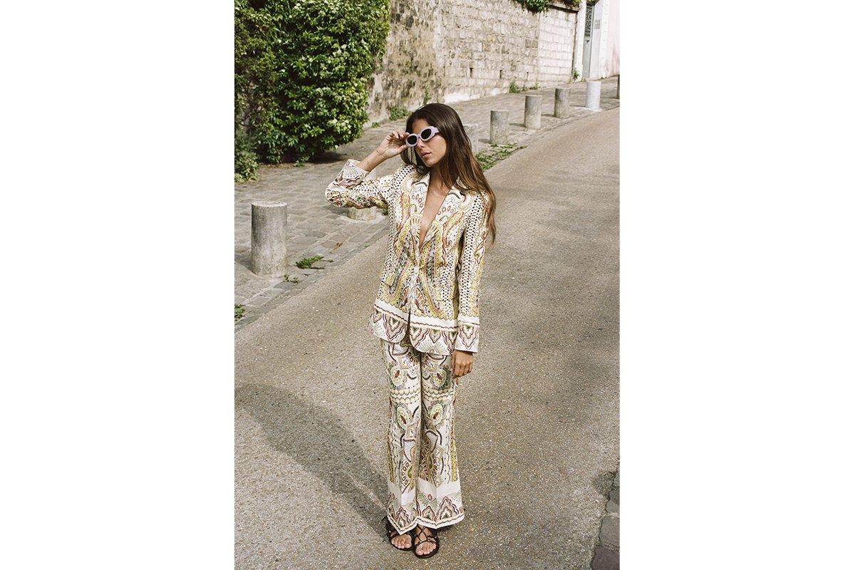 Chica castaña con el pelo suelto y gafas blancas en un exterior con un traje de pantalón y americana estampados