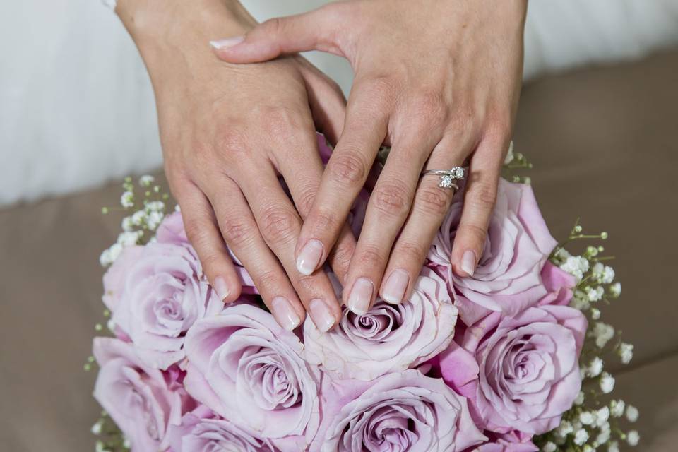 manos de mujer con manicura francesa clásica encima de un ramo de novia de flores rosas